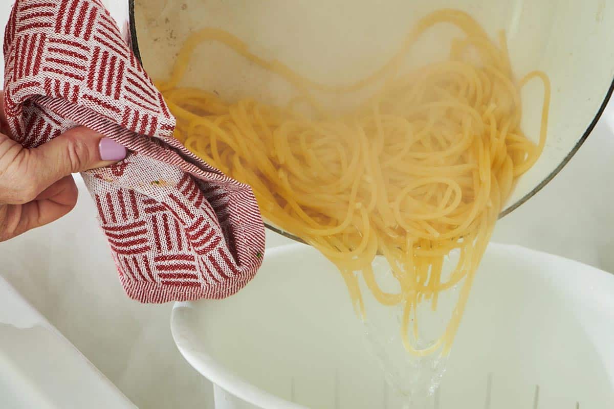 Pouring cooked spaghetti pasta from pot into colander.