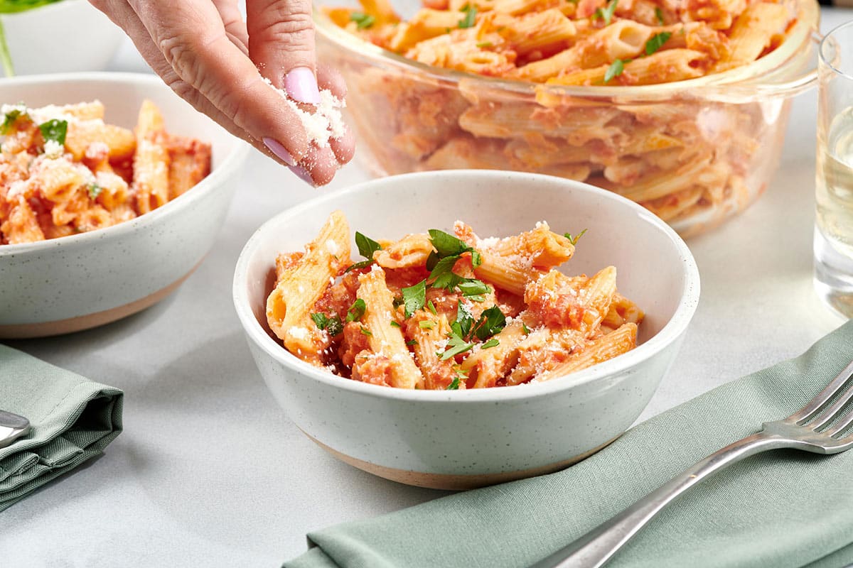 Woman sprinkling parmesan cheese onto a bowl of Penne alla Vodka.