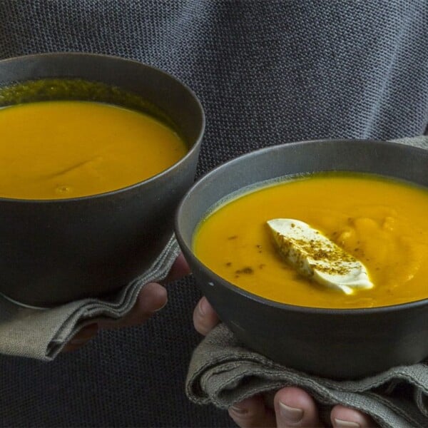 Woman holding two bowls of Indian Butternut Squash and Carrot soup.