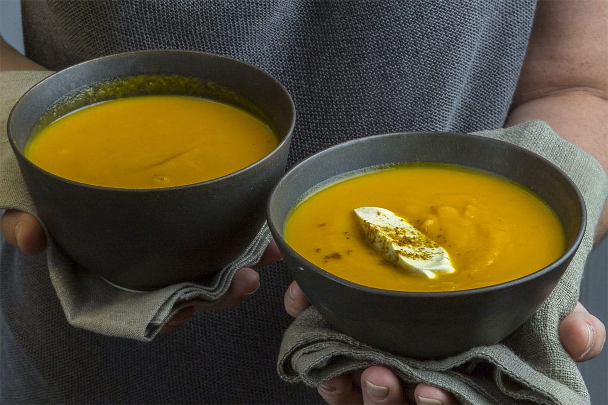 Woman holding two bowls of Indian Butternut Squash and Carrot soup.