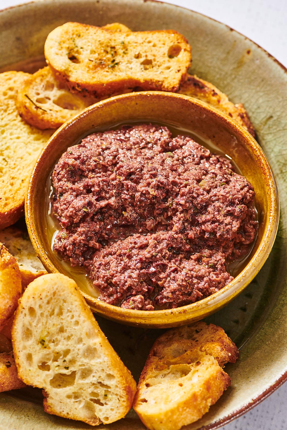 Bowl of Black Olive Tapenade on tray with crostini bread.