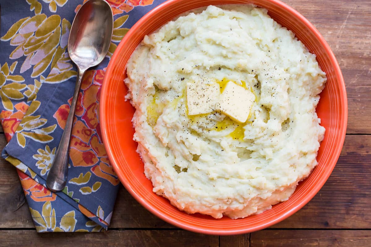 Bowl of Cheesy Mashed Potatoes topped with butter.