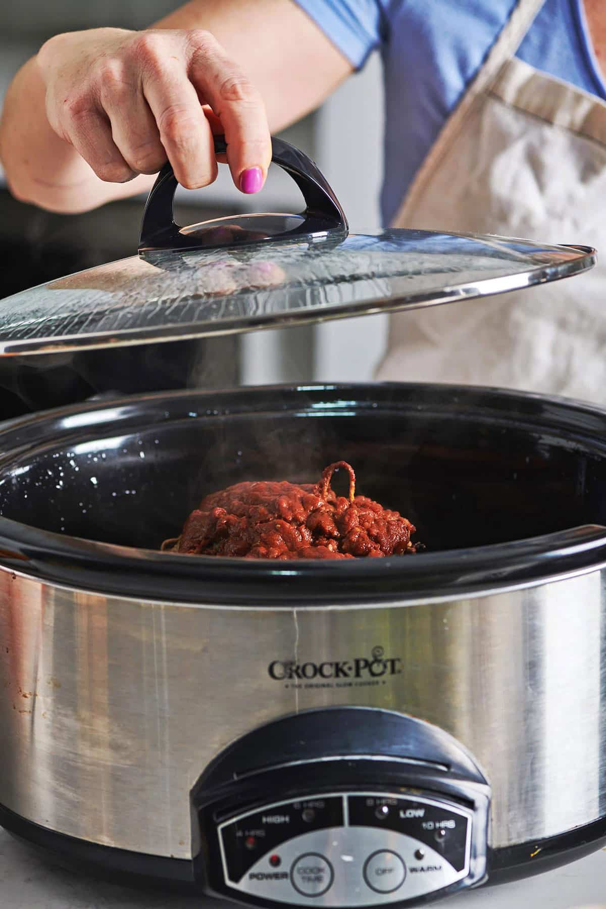 Woman lifting crockpot lid up with BBQ lamb in the pot.