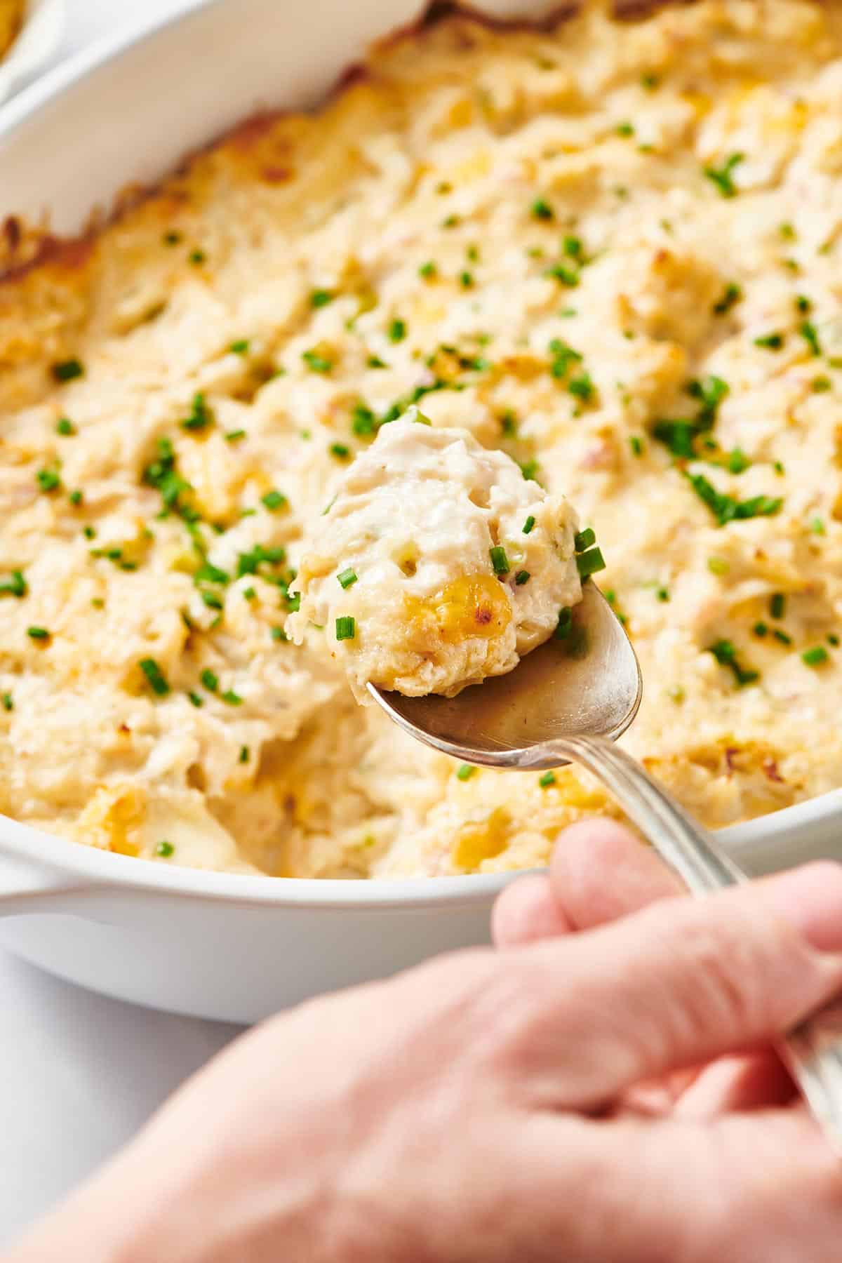 Woman scooping baked clam dip from dish with spoon.