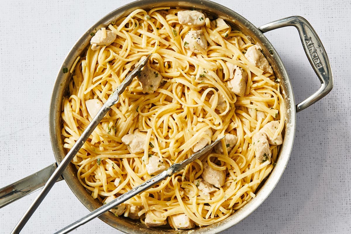 Chicken Alfredo in pan with tongs.