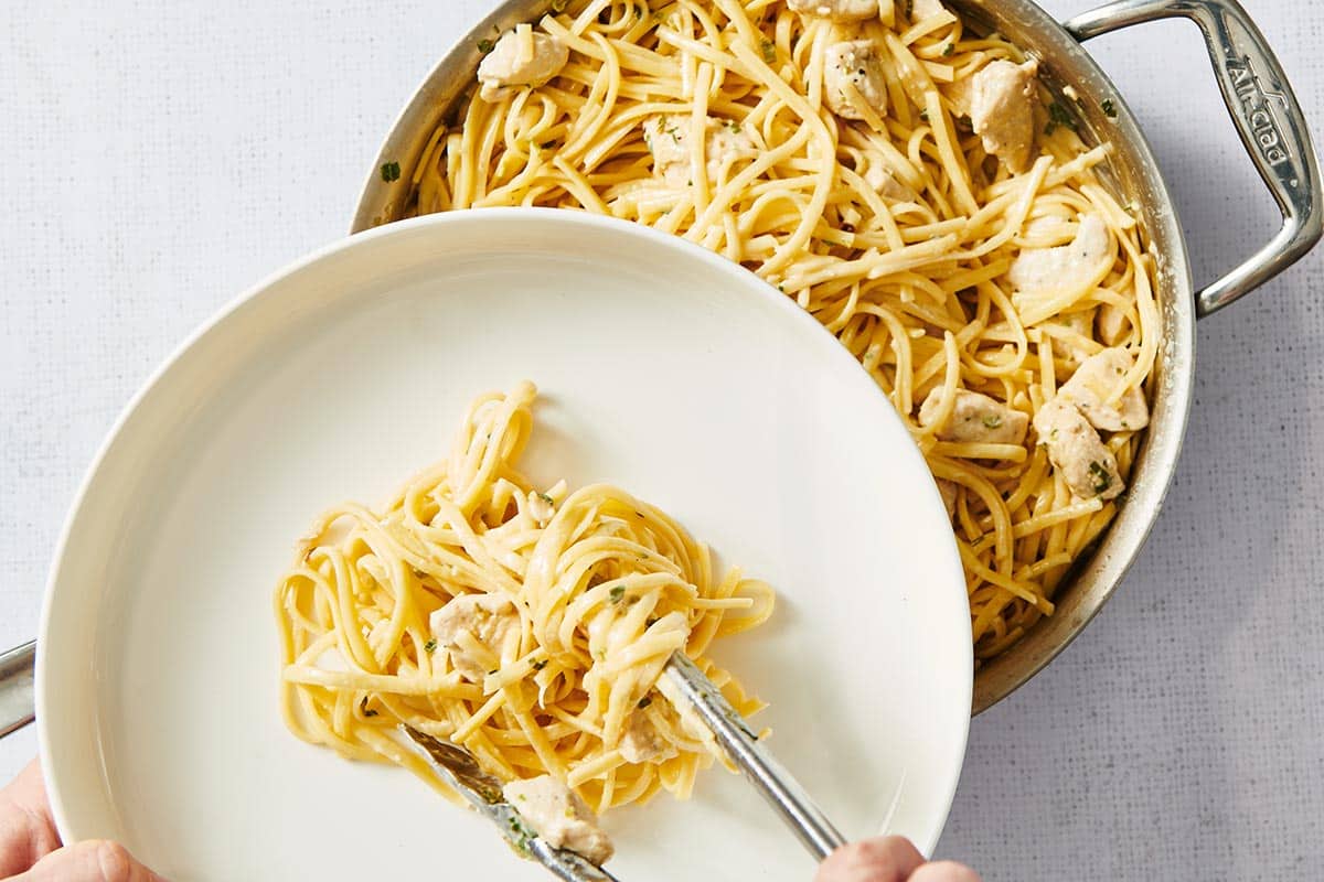 Serving chicken alfredo from white bowl with two forks.