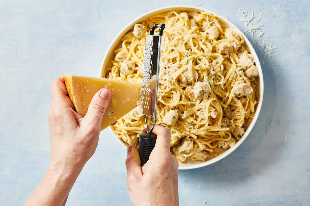 Woman grating Parmesan cheese over platter of Chicken Alfredo.