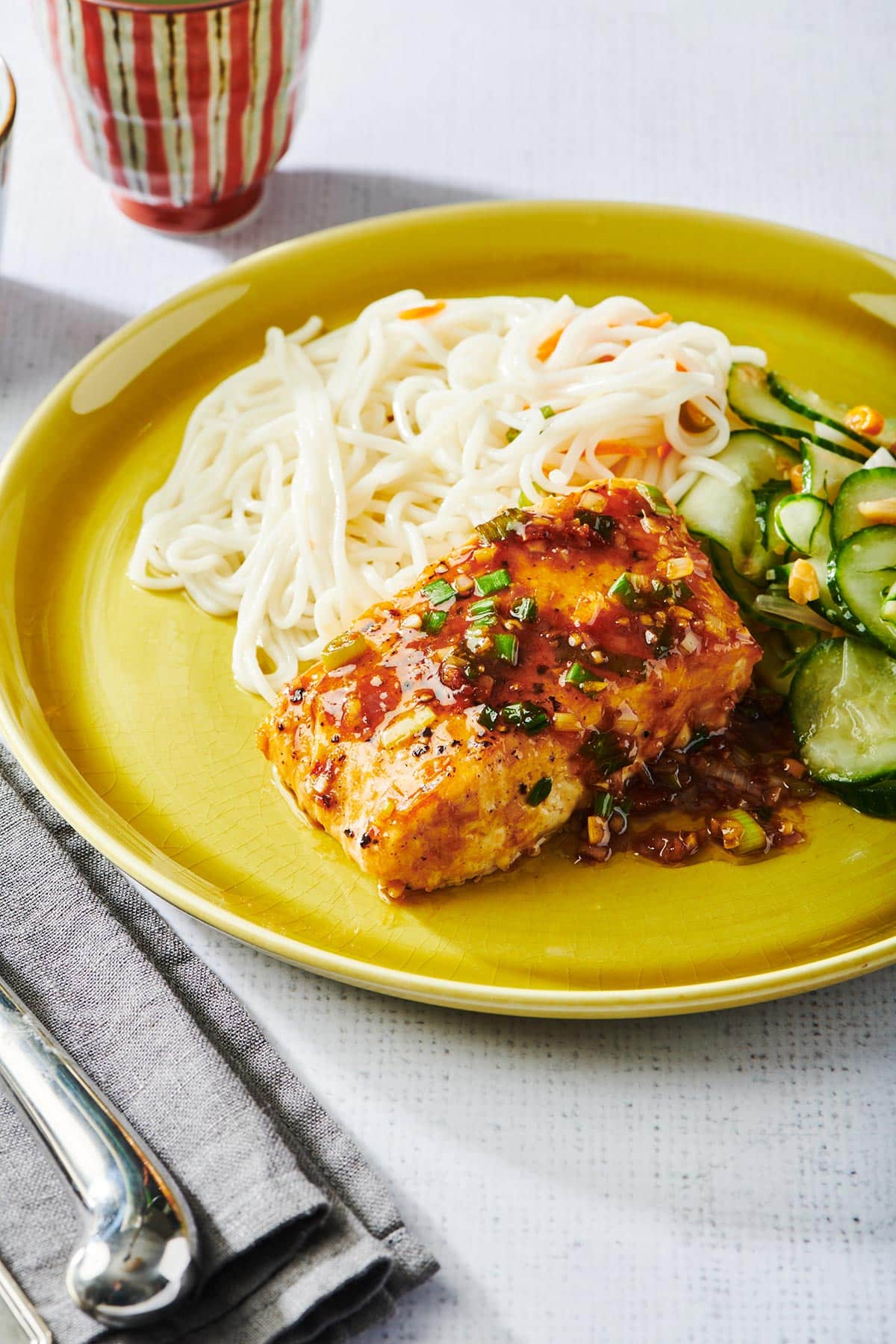 Ginger lemongrass salmon with noodles and cucumber salad on yellow plate.