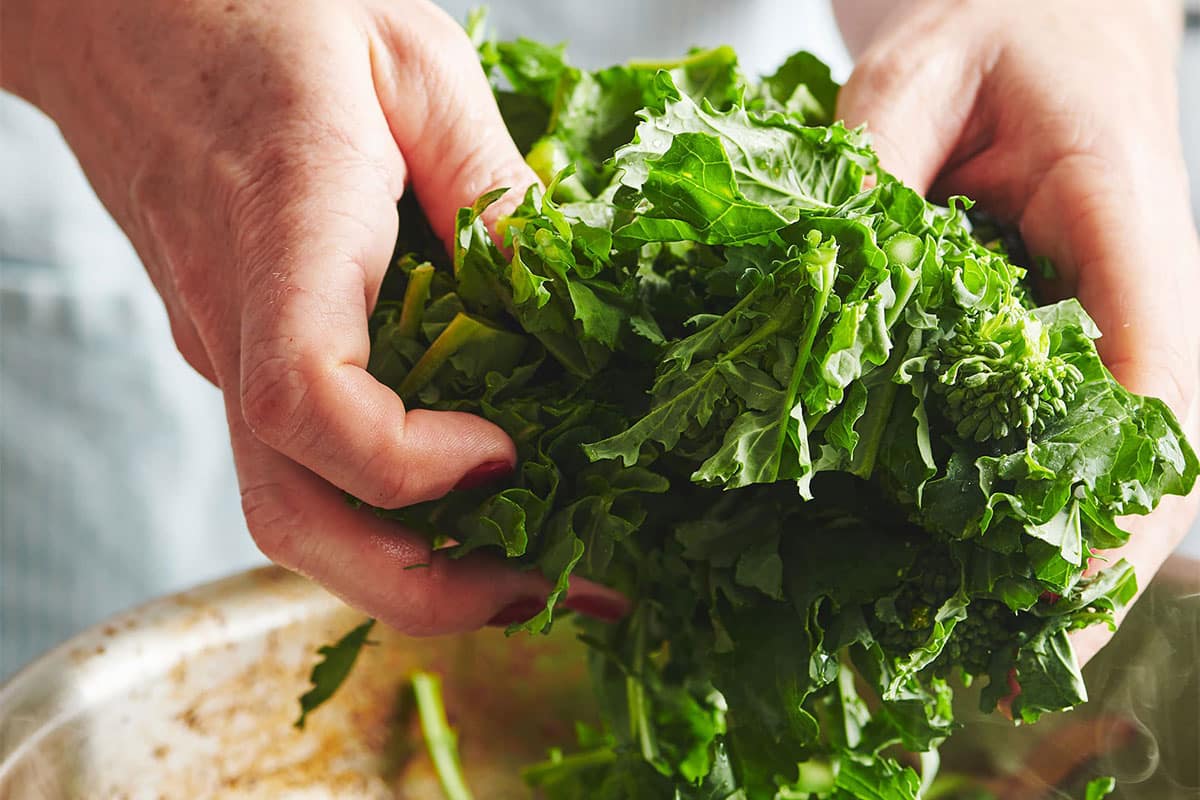 Woman placing fresh broccoli rabe in frying pan.