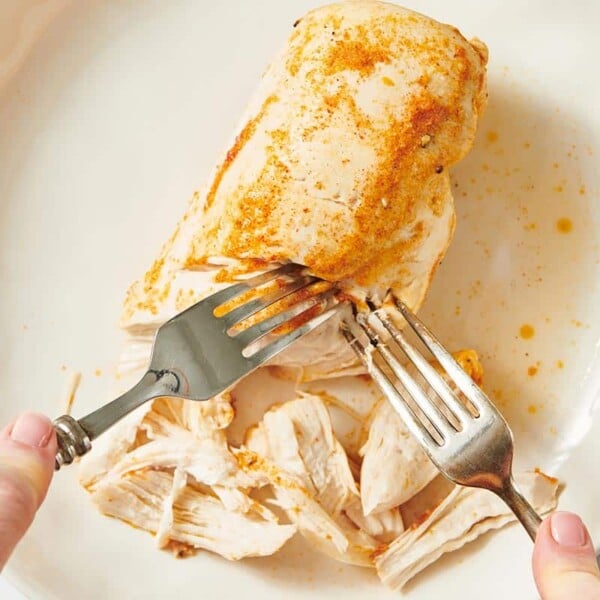 Shredding chicken breast cooked in instant pot with forks on white plate.