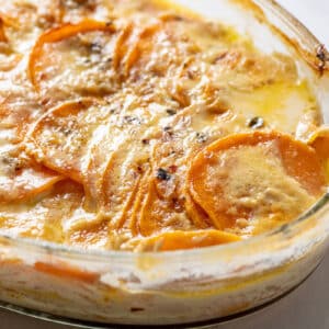 Creamy scalloped sweet potatoes in glass baking pan on table.
