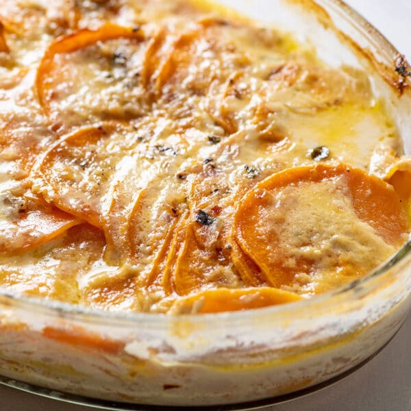 Creamy scalloped sweet potatoes in glass baking pan on table.