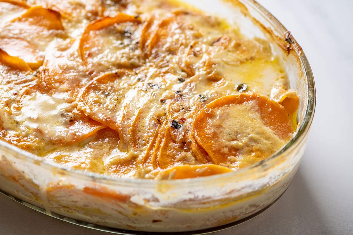 Creamy scalloped sweet potatoes in glass baking pan on table.