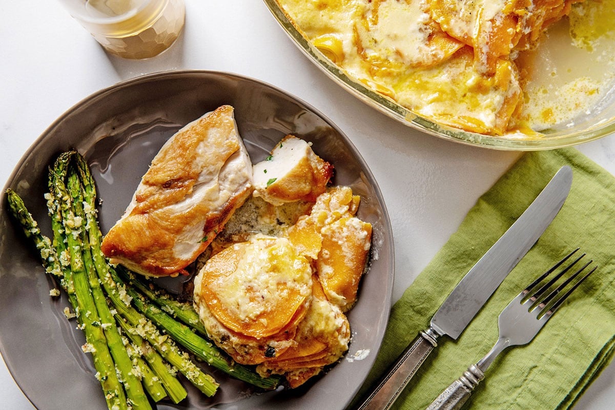 Scalloped Sweet Potatoes on plate with chicken and asparagus.