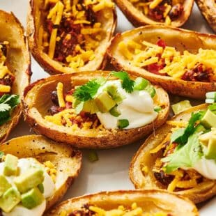 Vegan loaded potato skins with cilantro, avocado, and sour cream toppings on white plate.