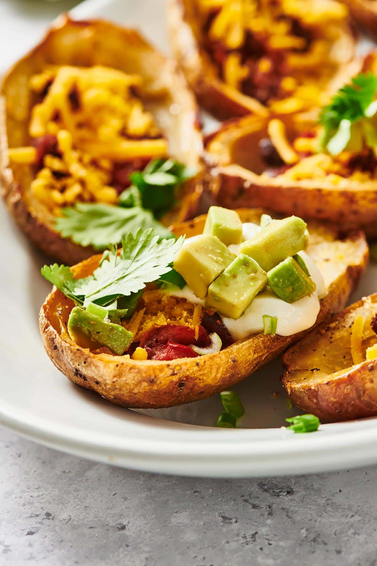 White plate filled with vegan loaded potato skins topped by avocado and cilantro.