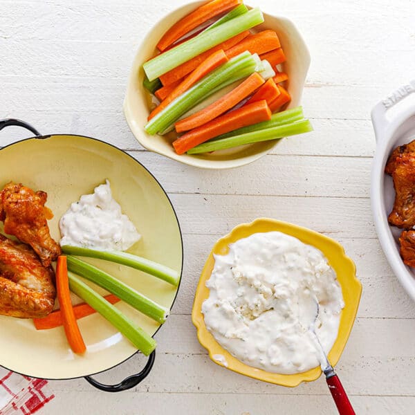 Buffalo chicken wings in plates and bowls with celery and carrot sticks, and ranch dip.