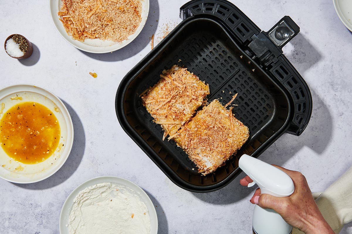 Spraying oil on breaded halibut filets in air fryer.