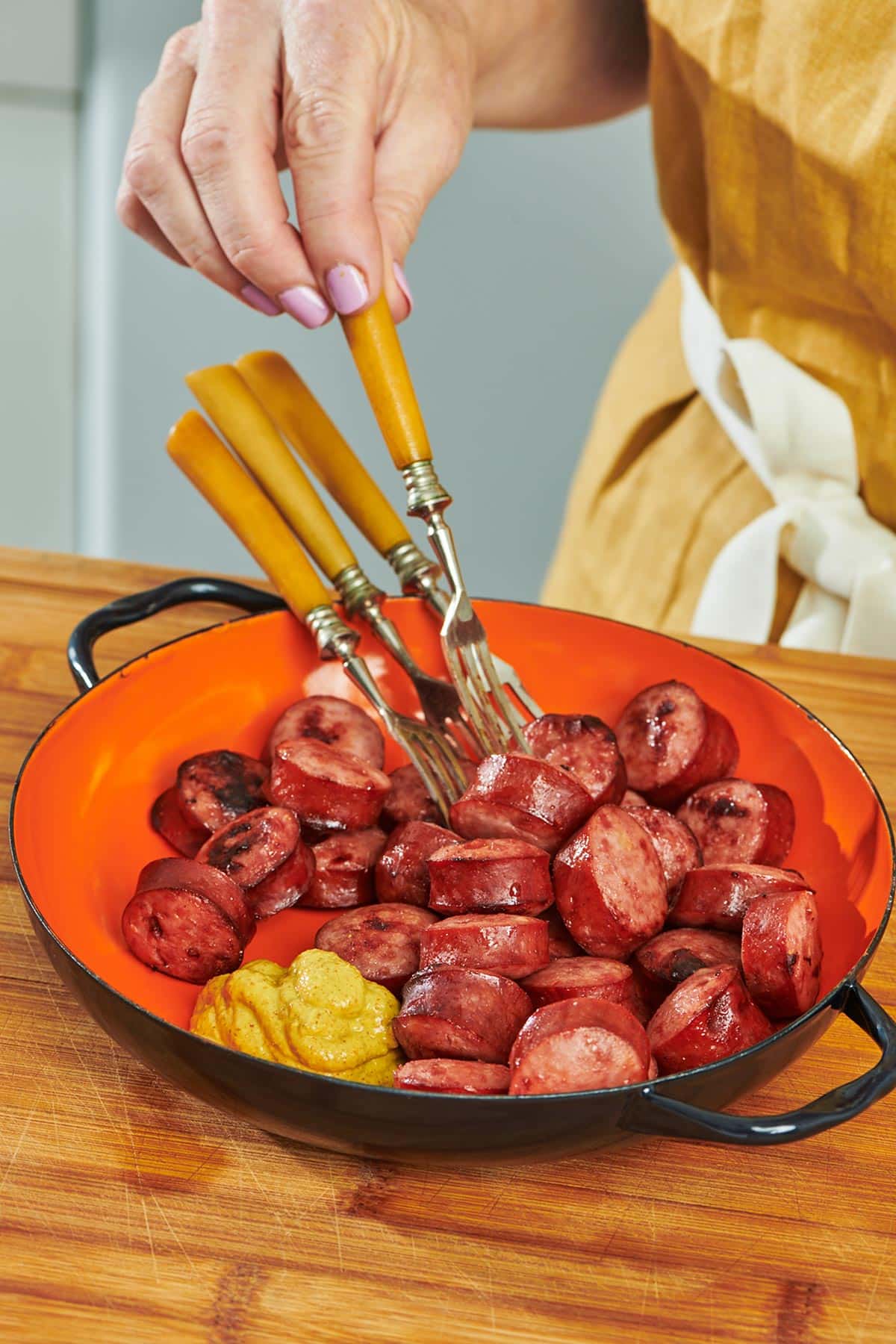 Woman serving air fried kielbasa and mustard with fork.