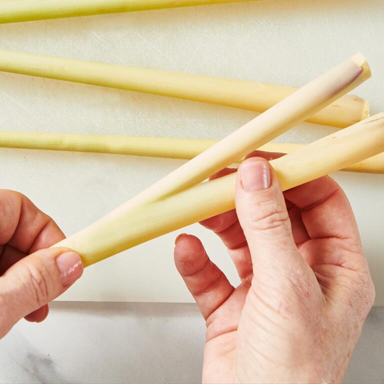 Woman peeling outer layer off lemongrass stalks over cutting board.