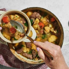 Woman scooping Irish Lamb Stew from cooking pot into bowl.