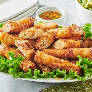 Fried Vietnamese spring rolls over bed of lettuce on plate.