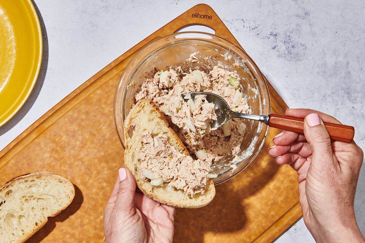 Scooping tuna fish onto bread with spoon.
