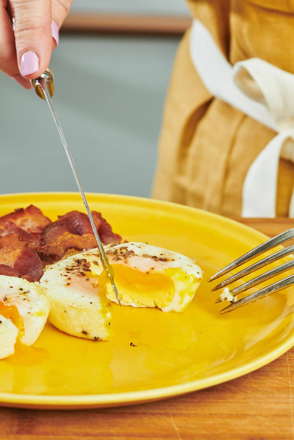 Slicing oven-baked egg with knife and fork on yellow plate.