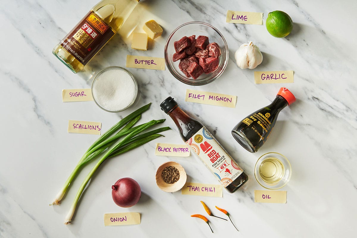 Beef, scallions, soy sauce, and other stir-fry ingredients on white marble table.