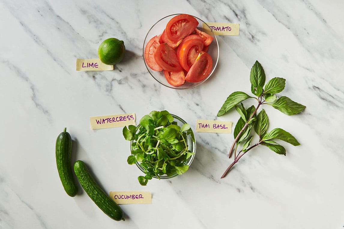Fresh watercress, cucumber, tomato, lime, and basil on white marble table.