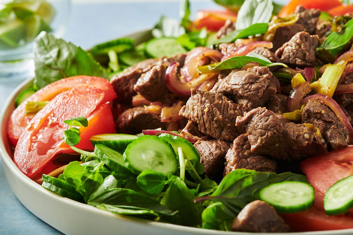 Shaking beef on plate with watercress, tomatoes, and other vegetables.