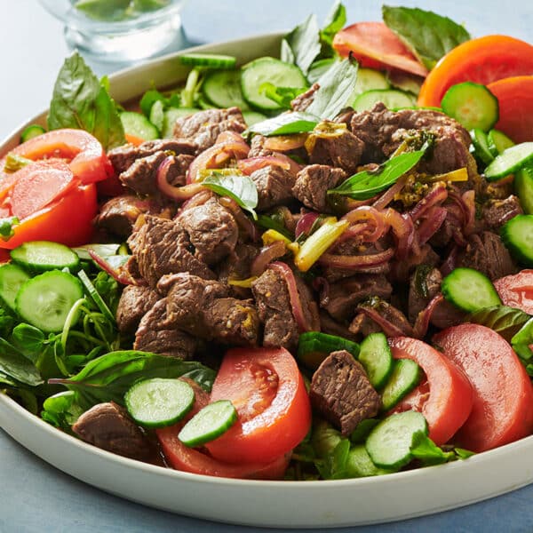 Stir-fried Vietnamese shaking beef on plate over bed of greens, tomatoes, and cucumbers.
