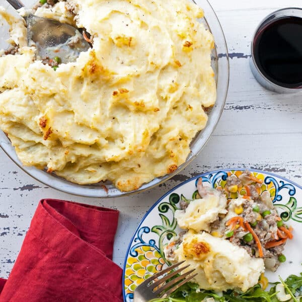 Shepherd’s Pie in pan and on plate on white wood table.