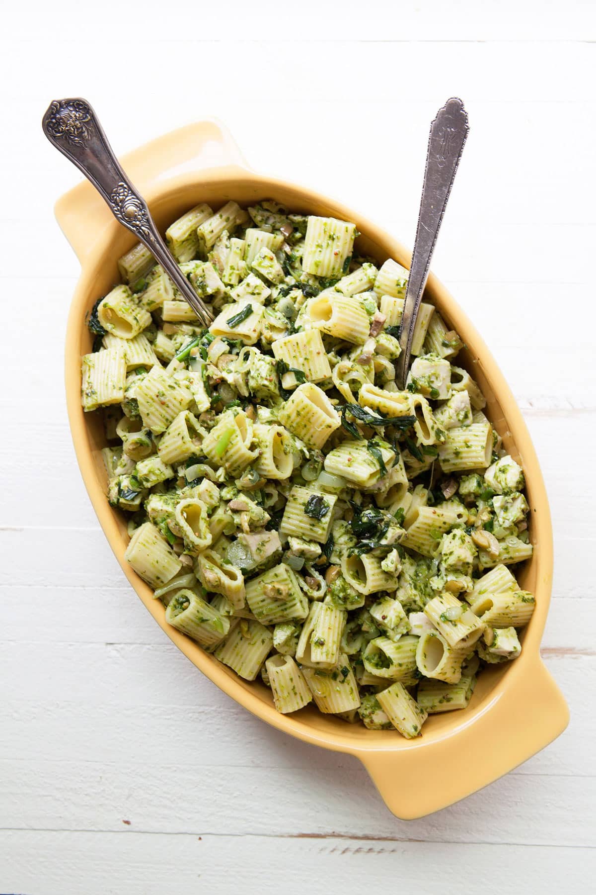 Yellow serving dish with ramp vinaigrette chicken pasta salad on table.