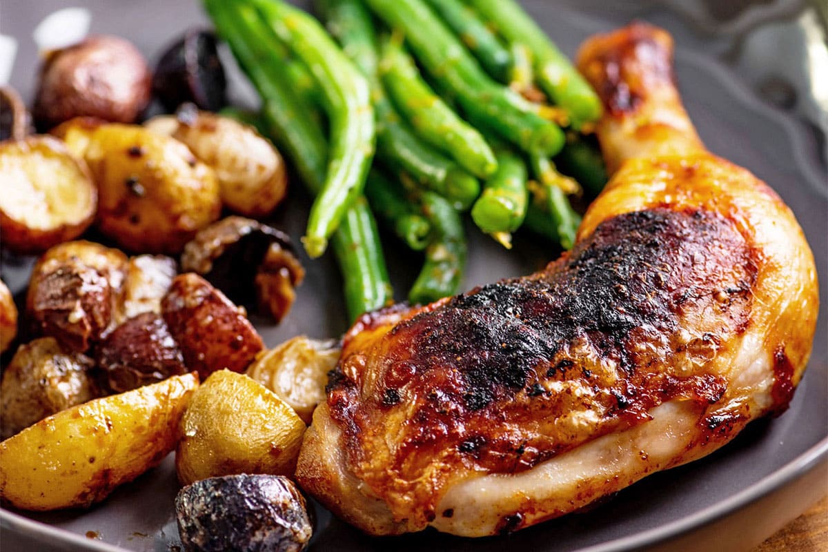 Baked Chicken Legs with Herbs and Lemon on a gray plate with green beans and potatoes.