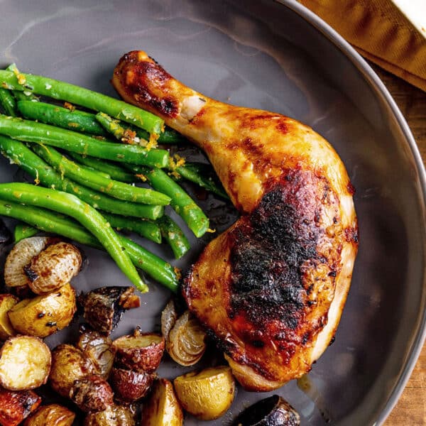 Roasted chicken leg on plate with green beans and potatoes.
