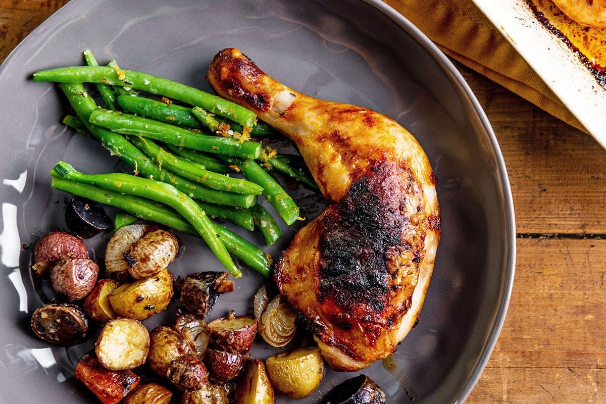 Roasted chicken leg on plate with green beans and potatoes.