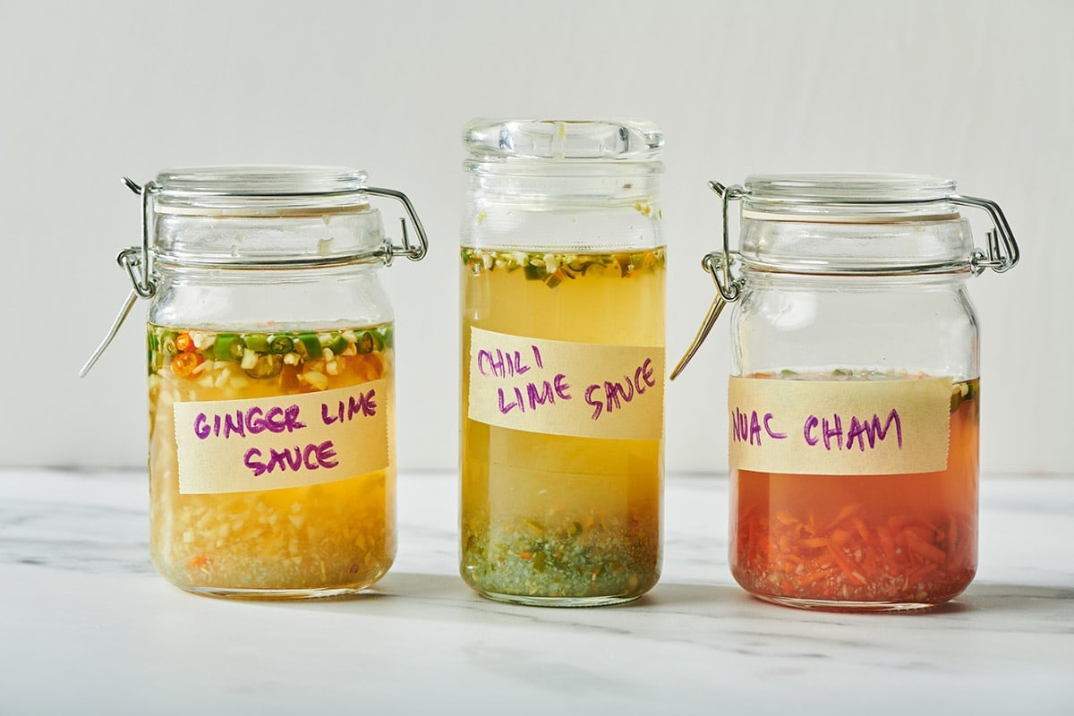Three variations of nuoc cham (chili lime sauce) in glass jars.