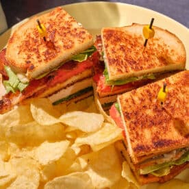 Club Sandwich on toasted bread with chips on yellow plate.