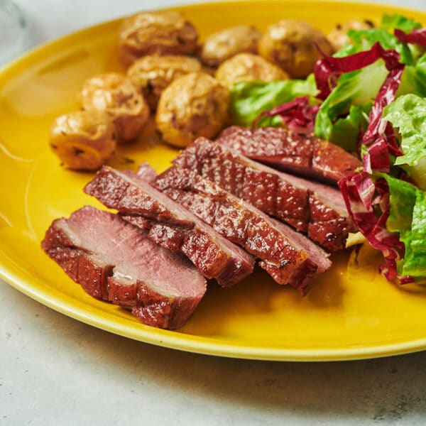 Sliced duck breast on yellow plate with salad and sides.