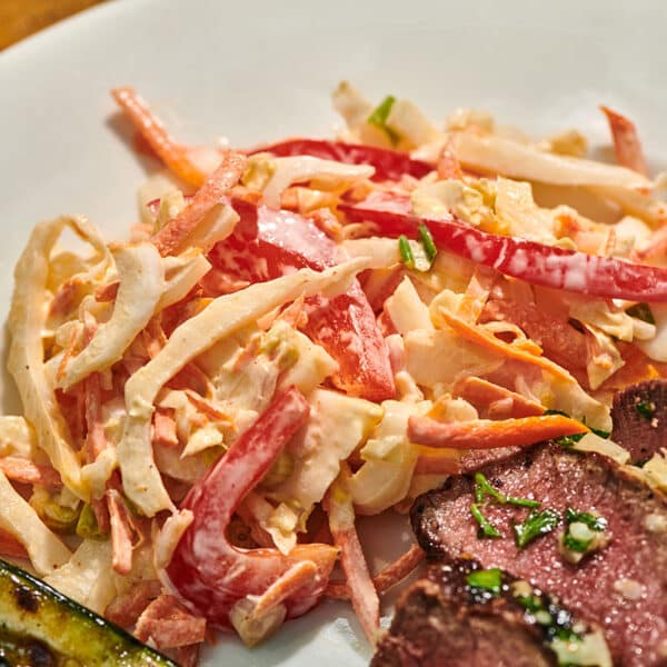 Old-fashioned coleslaw on plate with steak and grilled vegetables.