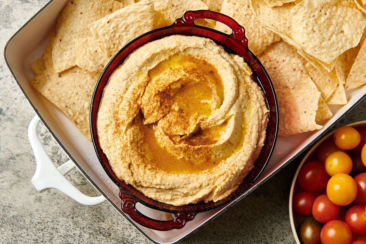 Tray with chips and bowl of hummus on table.