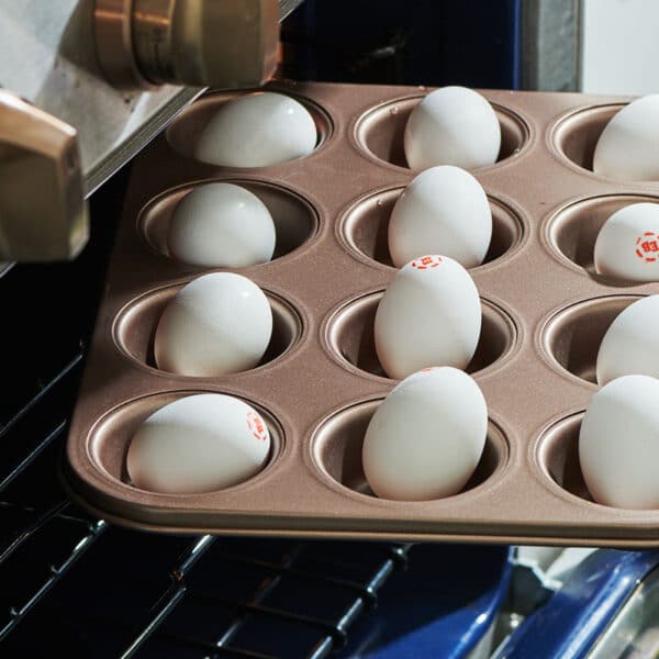 Placing muffin tin of raw eggs in oven for hard-boiled eggs.