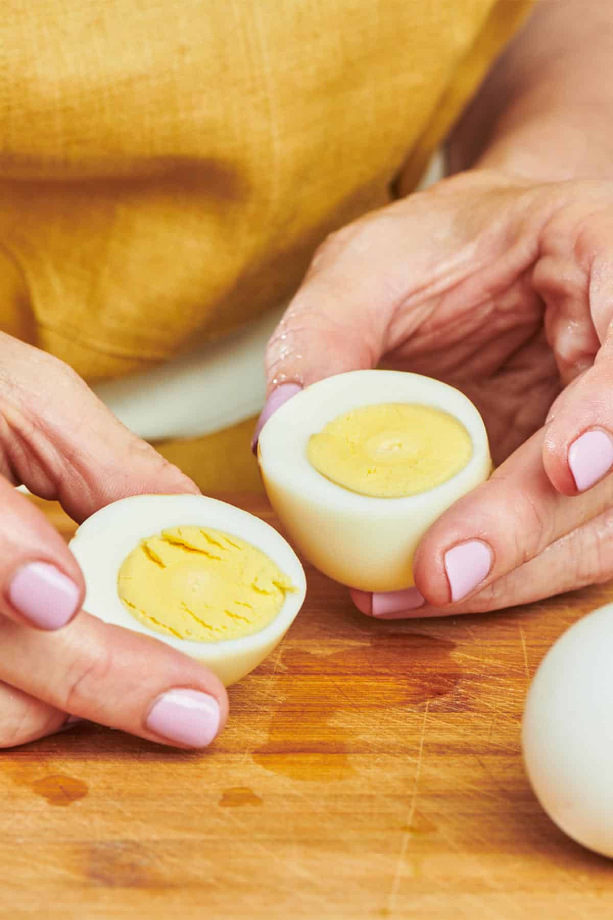 Woman holding cut hard-cooked egg on cutting board.