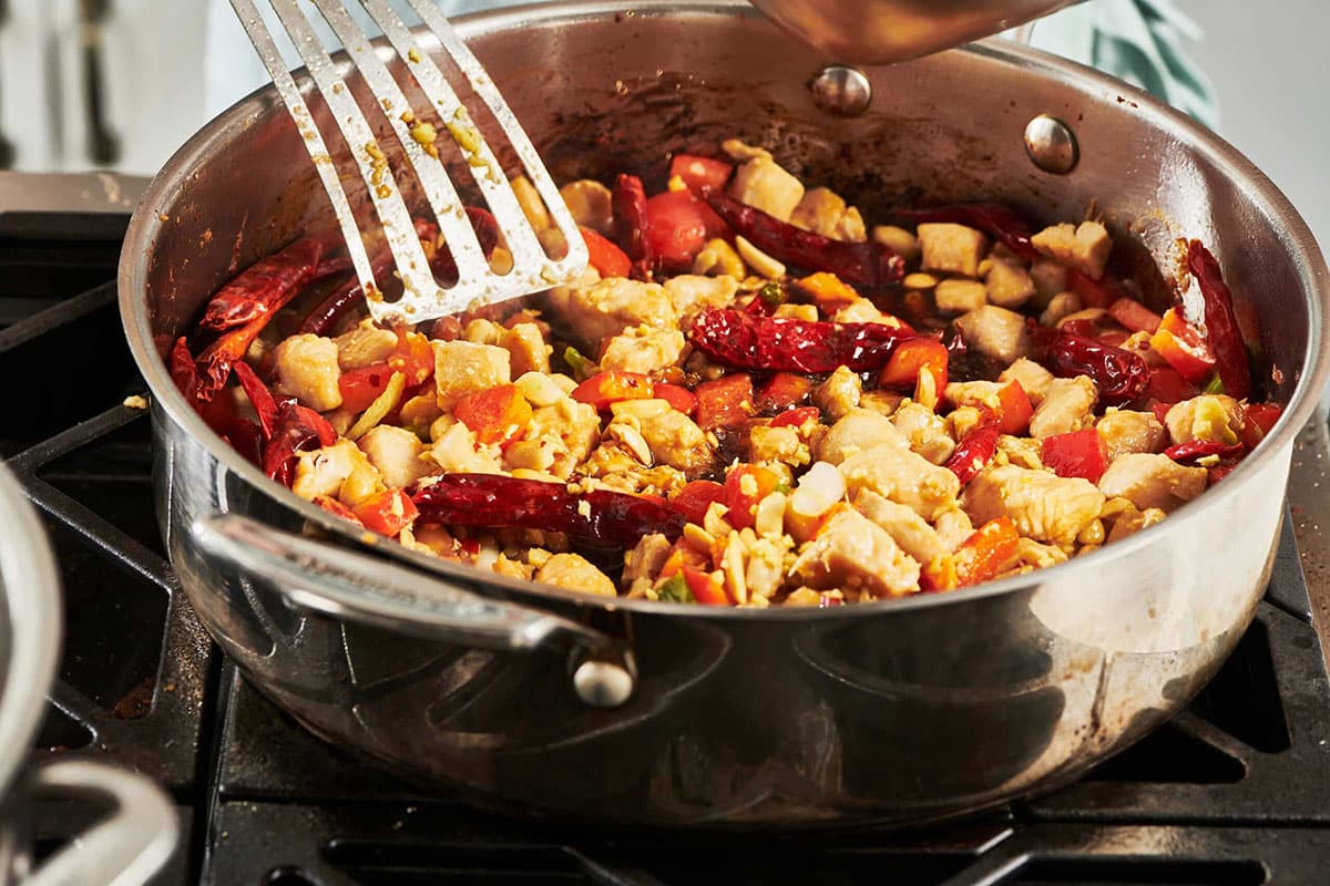 Metal spatula stirring a skillet of chicken and vegetables.