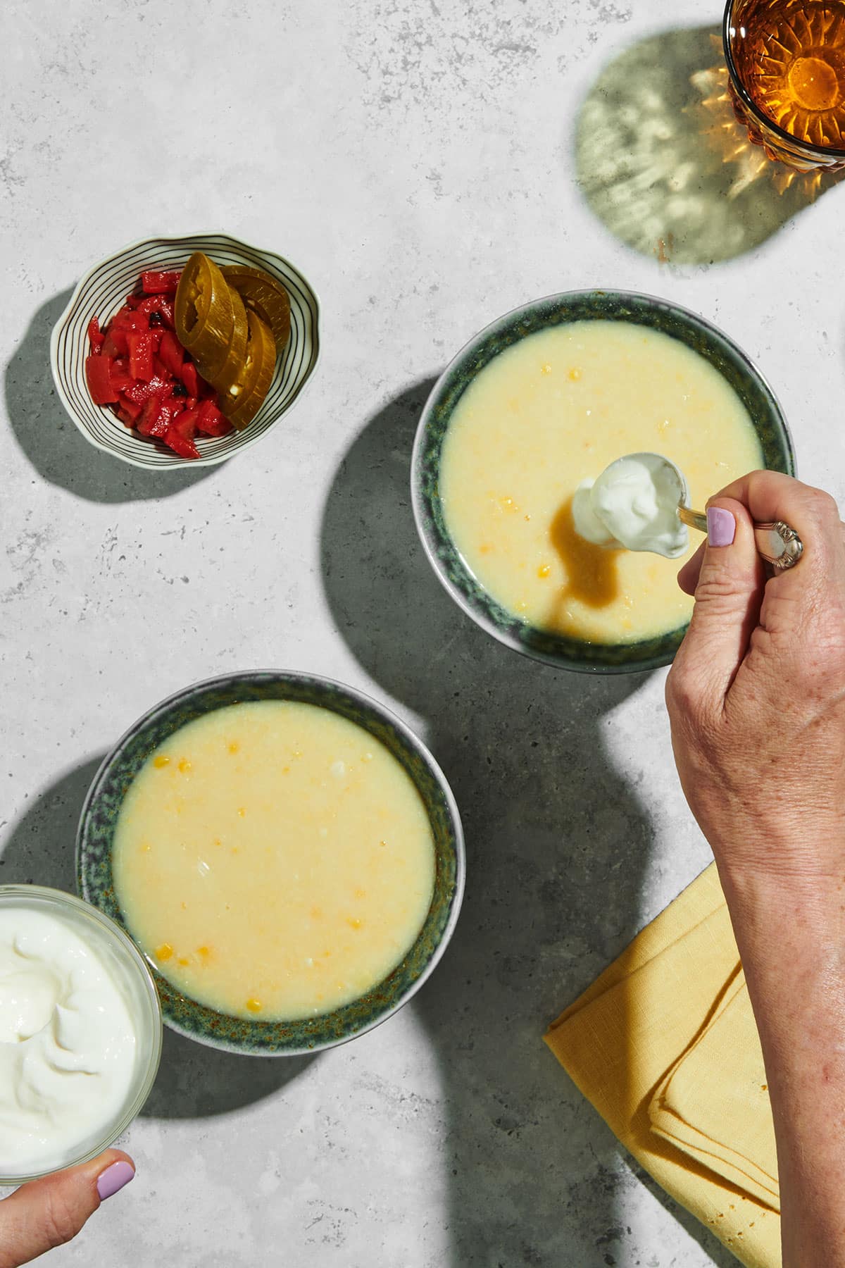 Adding sour cream on top of corn soup in bowls.