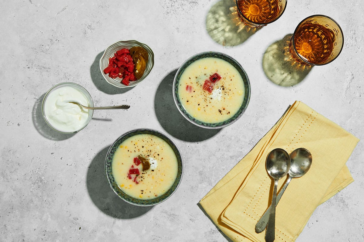 Creamy sweet corn soup in bowls topped with sour cream and peppers.