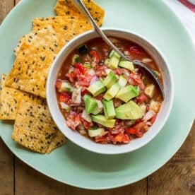Gazpacho in bowl on plate with chips.