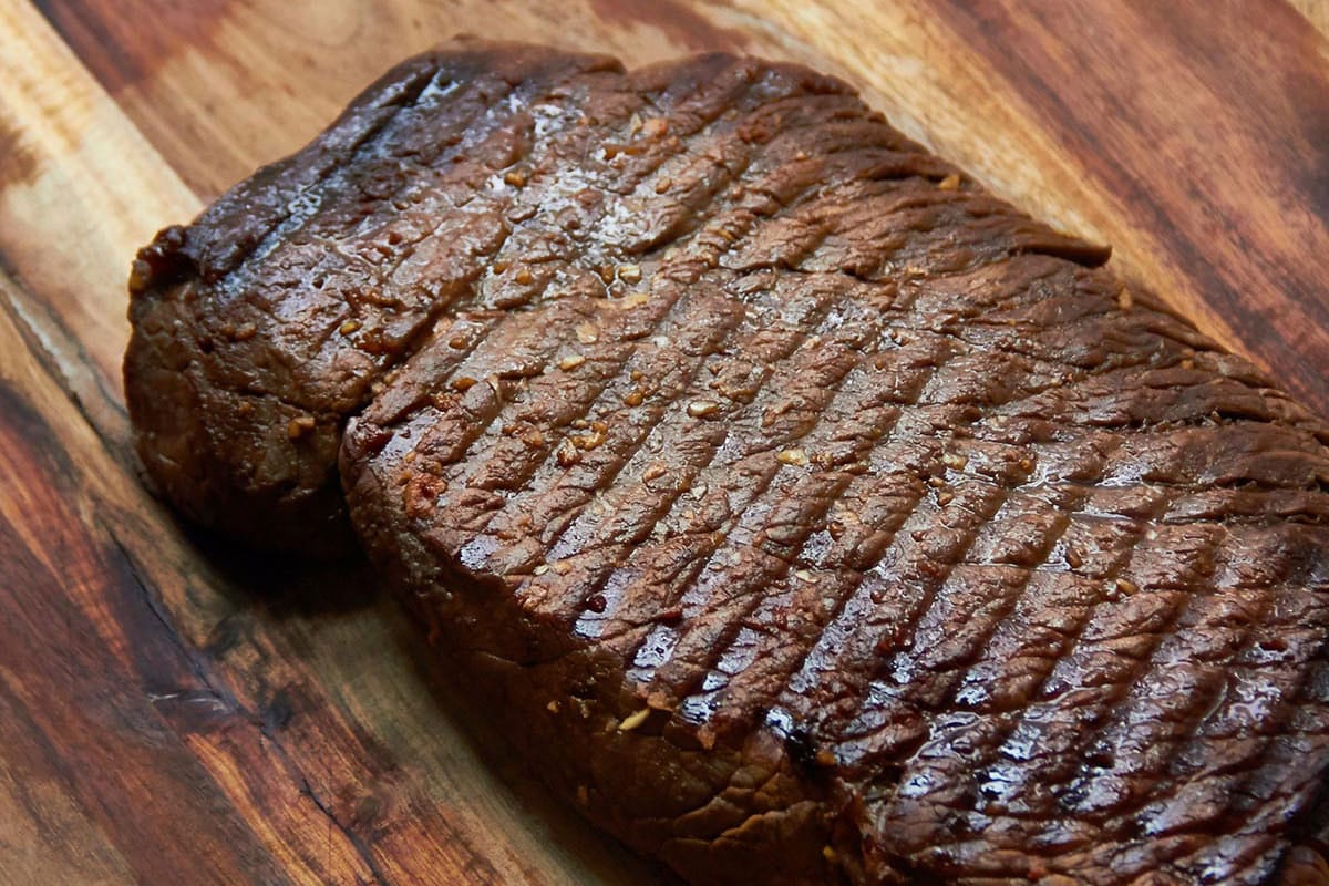 Grilled Marinated London Broil resting on a wooden surface.