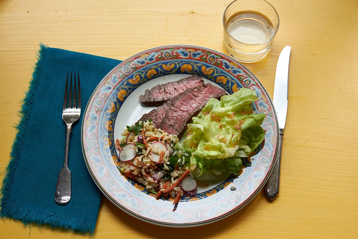Grilled Marinated London Broil on plate with sauce, rice, and salad.